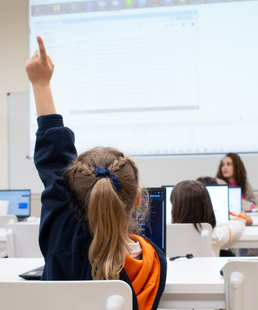 Niña levantando la mano para preguntar en clase de informática en primaria