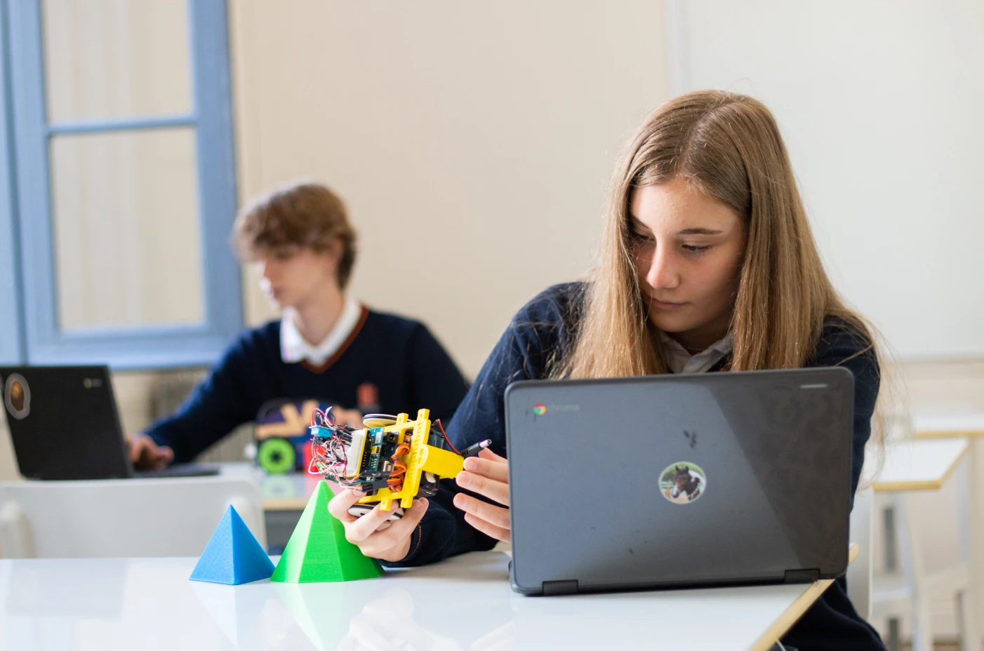 instituto concertado: alumna trabajando con un portátil y un robot educativo en una actividad de tecnología en el aula